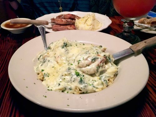 A plate of creamy pasta topped with shrimp and herbs, with a side of meat and mashed potatoes in the background.