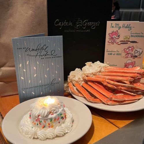 A birthday card, a plate of crab legs, and a dessert with a candle on a table at a seafood restaurant.