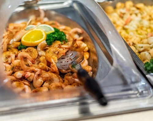 A serving dish filled with cooked shrimp garnished with lemon slices and parsley, next to another seafood dish.
