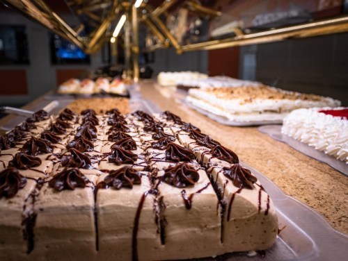 A variety of desserts displayed on a buffet, featuring layered cakes and chocolate drizzles.