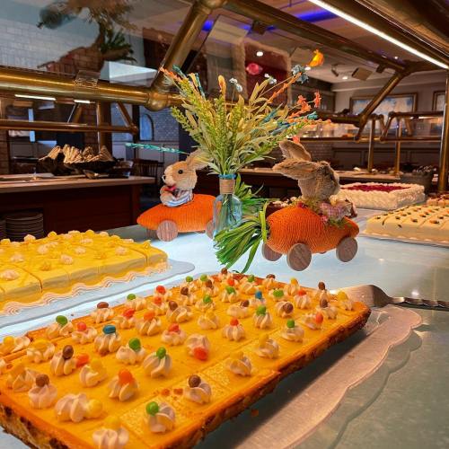 A colorful dessert display featuring cakes and a floral centerpiece with bunny figurines in toy cars.