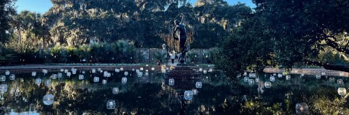 A serene pond with floating lanterns, featuring a central statue surrounded by lush greenery and trees.