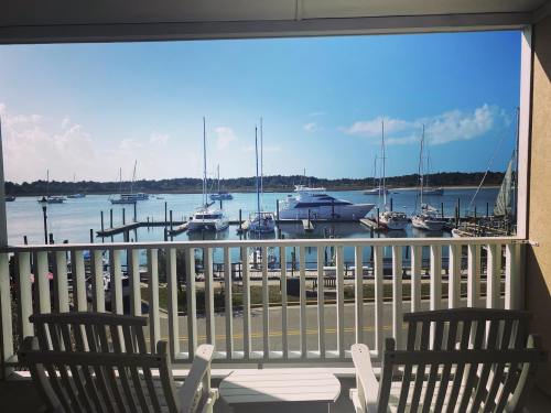 View from a balcony overlooking a marina with sailboats and yachts under a clear blue sky. Two rocking chairs in foreground.