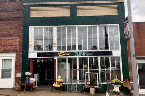 A storefront with large windows, painted green and brick, featuring a sign that reads "Union JUNKtion" and an open sign.