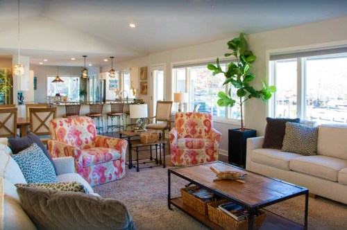 Bright living room with colorful chairs, a cozy sofa, and large windows, featuring a coffee table and decorative plants.
