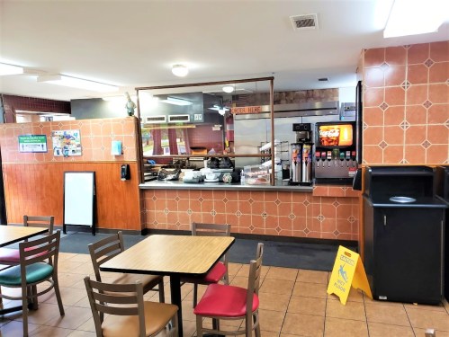 A casual dining area with a counter, drink station, and tables, featuring tiled walls and a clean, inviting atmosphere.