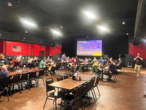 A spacious dining area with tables filled with people watching a large screen, featuring a sports event.