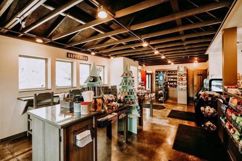 A cozy café interior with wooden tables, a festive display, and shelves filled with various products. Bright and inviting atmosphere.