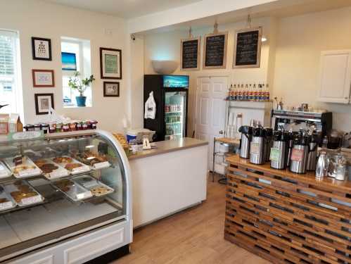 A cozy café interior featuring a display case of pastries, a coffee station, and a fridge with drinks.