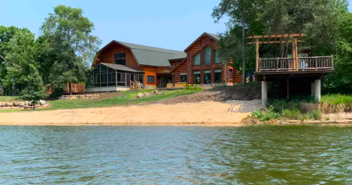 Sprawling riverfront log home with a sandy beach and elevated deck at a cabin rental in Iowa.