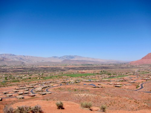 A panoramic view of a desert landscape with mountains in the background and scattered green areas and homes below.