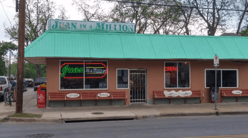 Exterior of "Juan in a Million" restaurant with a green roof, neon signs, and benches outside. Open for business.