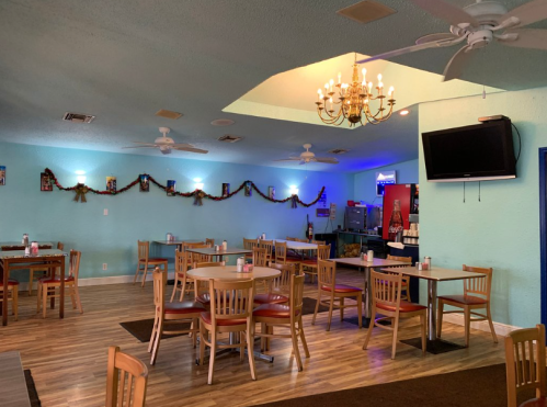 A cozy restaurant interior with wooden tables, chairs, a chandelier, and festive decorations on the walls.