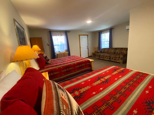 Cozy hotel room with two beds, colorful blankets, a couch, and natural light from windows.