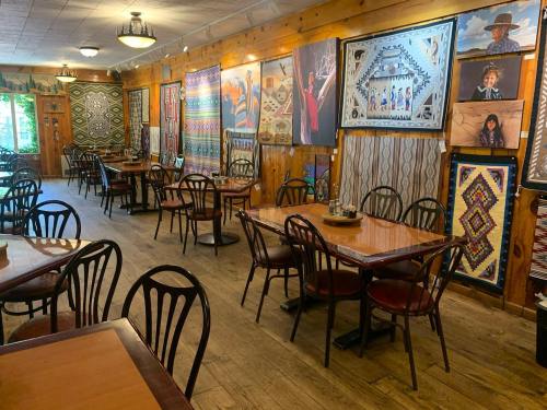 A cozy dining area with wooden walls, decorated with colorful artwork and patterned textiles, featuring empty tables and chairs.