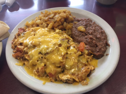 A plate of cheesy scrambled eggs with diced vegetables, served with seasoned potatoes and refried beans.