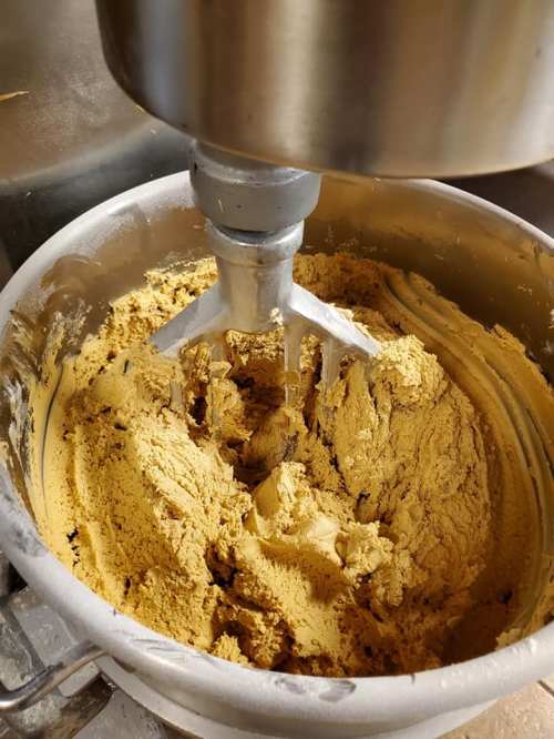 A close-up of a mixing bowl with thick, golden-brown dough being mixed by a stand mixer.