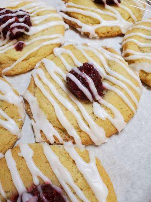 Close-up of cookies drizzled with icing and topped with a dollop of red fruit jam on a parchment-lined tray.