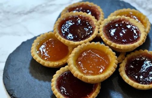 A close-up of assorted fruit tarts with glossy fillings on a dark slate plate.