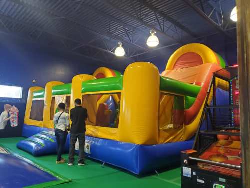 A colorful indoor bounce house with slides, surrounded by children and adults enjoying the space.