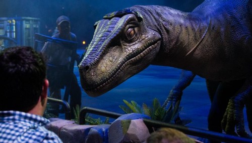 A lifelike dinosaur animatronic interacts with an audience in a dark, themed environment.