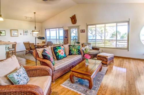 Cozy living room with wicker furniture, colorful cushions, a wooden coffee table, and large windows letting in natural light.