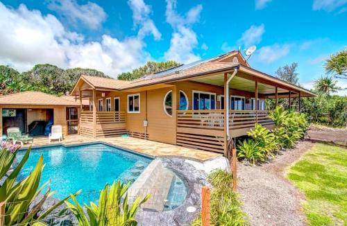A charming house with a pool surrounded by greenery, under a bright blue sky with fluffy clouds.