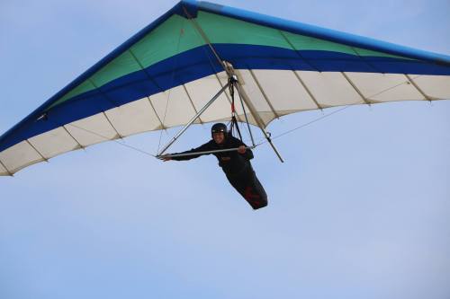 A person hang gliding in a blue and green wing against a clear sky.