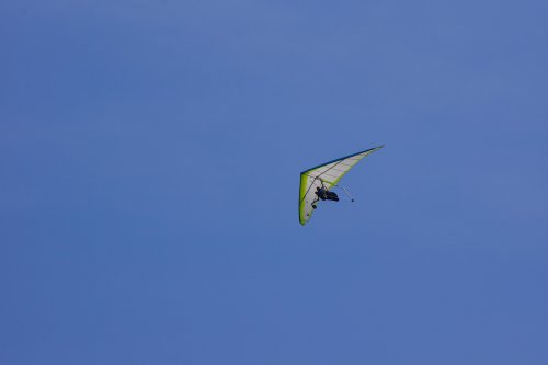 A hang glider soaring through a clear blue sky on a sunny day.