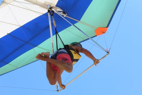 A person hang gliding in a colorful sail, suspended in the air against a clear blue sky.