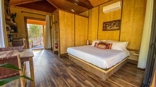 Cozy interior of a cabin featuring a queen bed, wooden decor, and large windows overlooking a forest.