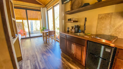 Cozy interior of a cabin featuring a kitchenette, dining area, and large windows overlooking a deck.