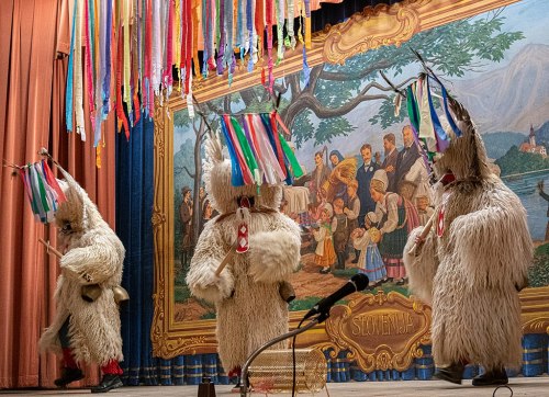 Three performers in furry costumes with colorful masks dance on stage, decorated with ribbons and a scenic backdrop.