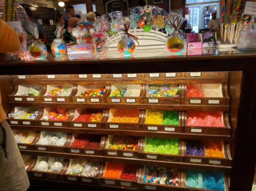 A colorful candy display with various jars filled with sweets in a wooden cabinet.