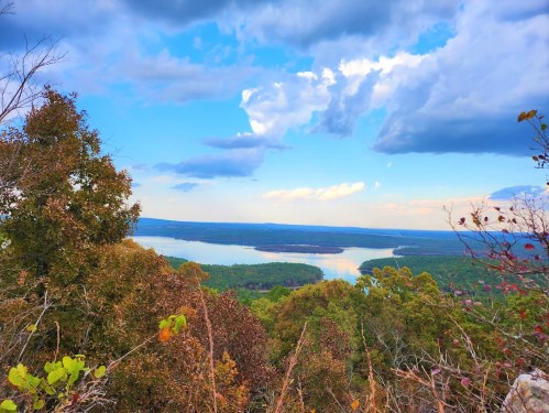 A scenic view of a lake surrounded by lush greenery and trees, under a partly cloudy sky.