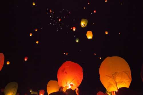 Colorful lanterns float into a dark night sky, illuminating the scene with warm hues of red, orange, and yellow.