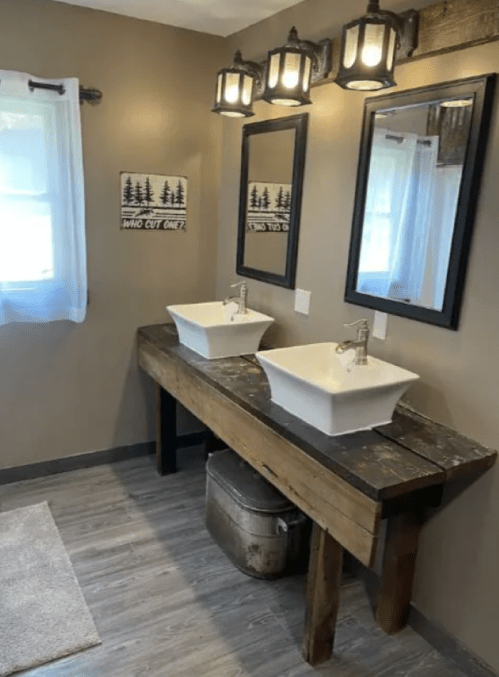 A rustic bathroom with two sinks on a wooden vanity, mirrors above, and warm lighting.