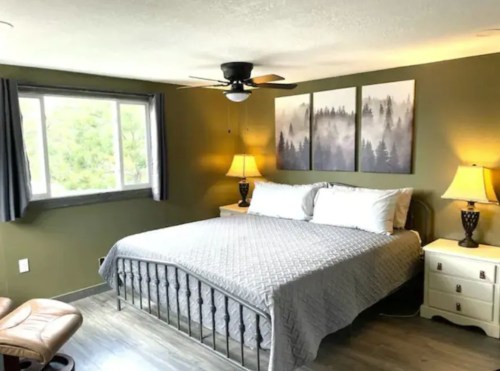 Cozy bedroom with a large bed, two lamps, and nature-themed artwork on the walls, featuring a window with a view.