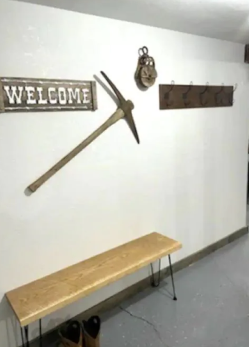 A rustic entryway featuring a "Welcome" sign, a pickaxe, a wall-mounted coat rack, and a wooden bench.