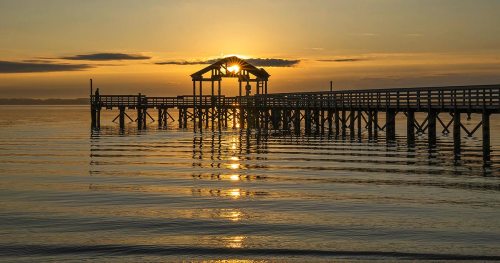 Sunset over a calm lake, with a wooden pier extending into the water, reflecting golden light.