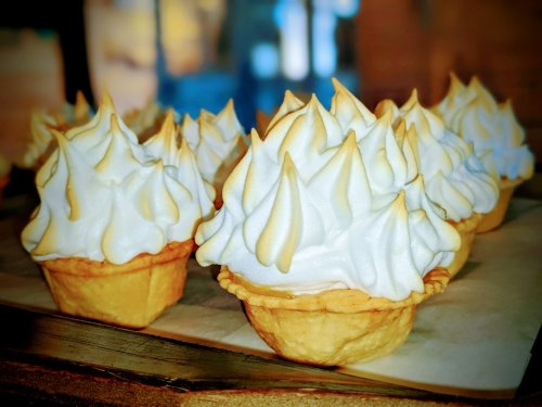 Close-up of dessert cups filled with fluffy, golden-brown meringue atop a light pastry shell.
