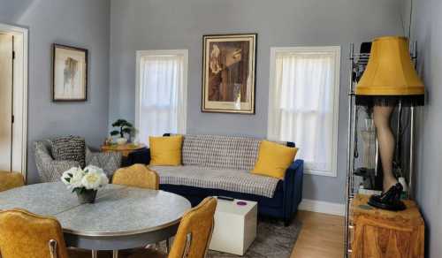 Cozy living room with a blue couch, round dining table, and a unique lamp featuring a leg design. Bright and inviting space.