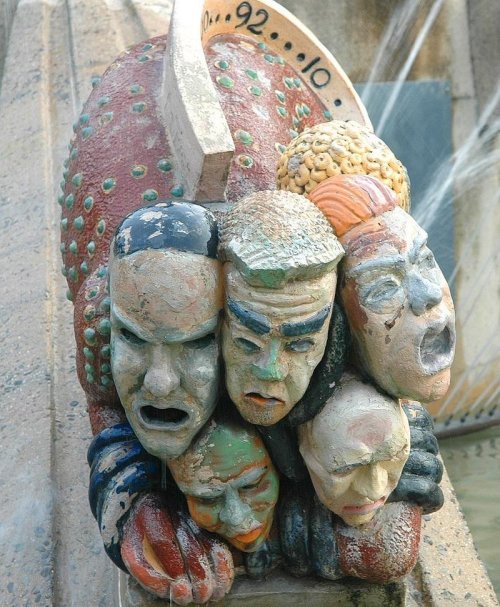 A colorful sculpture featuring four expressive faces, each showing different emotions, with water flowing around them.