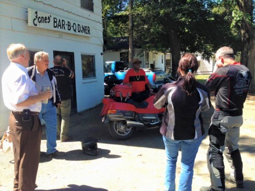 A group of people converses outside a barbecue restaurant, with a motorcycle parked nearby.