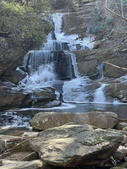 A serene waterfall cascades over rocky cliffs, surrounded by lush greenery and icy formations.
