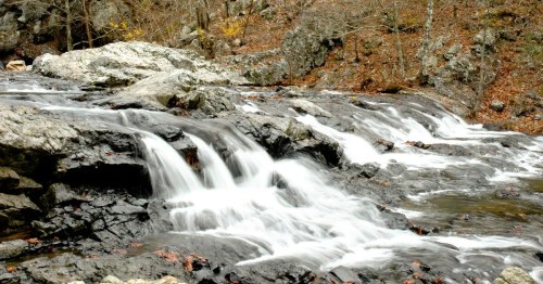 A serene waterfall cascading over rocky terrain, surrounded by autumn foliage and a tranquil forest setting.