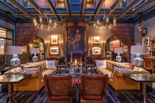 Elegant lounge with a high ceiling, vintage decor, plush seating, and a large portrait above a fireplace. Warm ambiance.