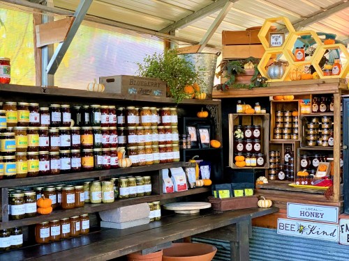 A rustic market stall displaying jars of preserves, honey, and seasonal decorations like pumpkins.