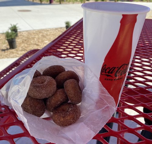 A bag of mini donuts next to a large cup of Coca-Cola on a red outdoor table.