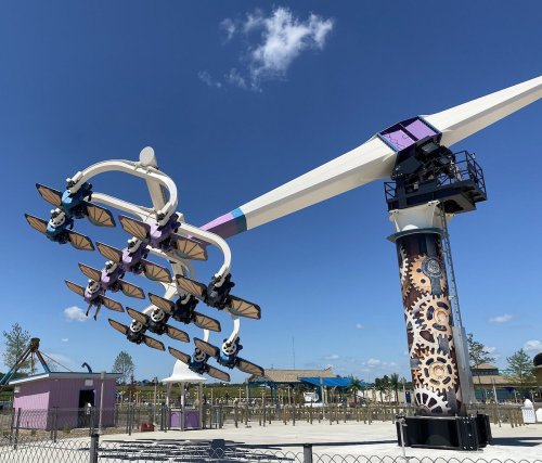 A large amusement park ride with seats suspended from a rotating arm against a clear blue sky.